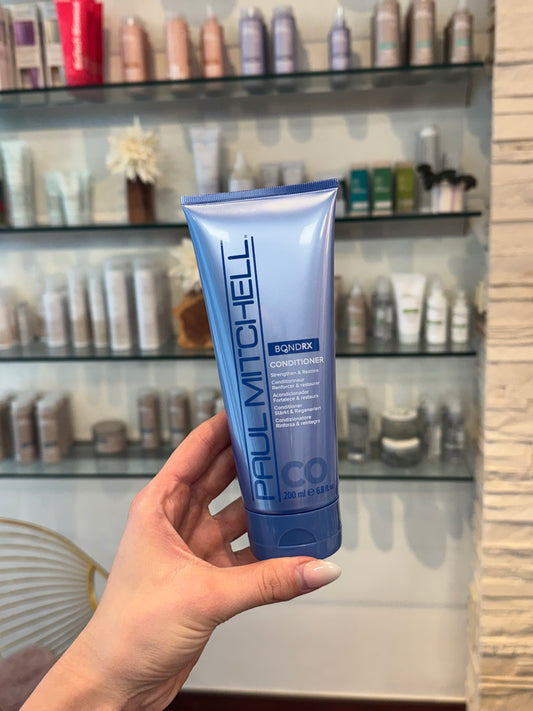 Bond Rx Conditioner für geschädigtes Haar, blaue Tube im Salon vor Produktregal gehalten – Paul Mitchell