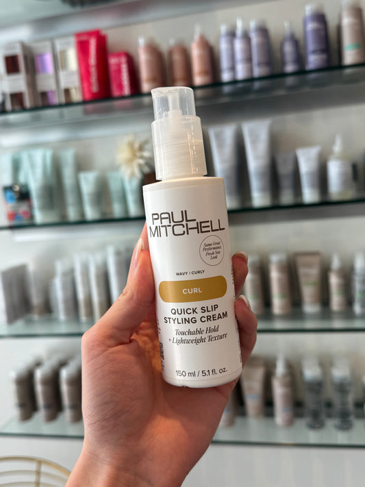 Paul Mitchell Curl Quick Slip Styling Cream – Stylingcreme für Locken in der Hand vor Produktregal fotografiert – Paul Mitchell