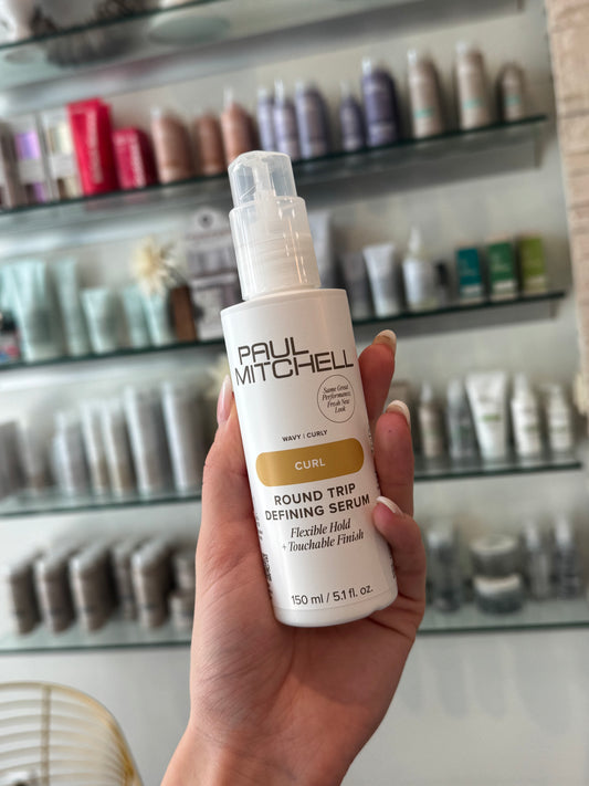     Paul Mitchell Curl Round Trip Defining Serum – Lockenserum in der Hand im Friseursalon mit Produktregal im Hintergrund – Paul Mitchell
