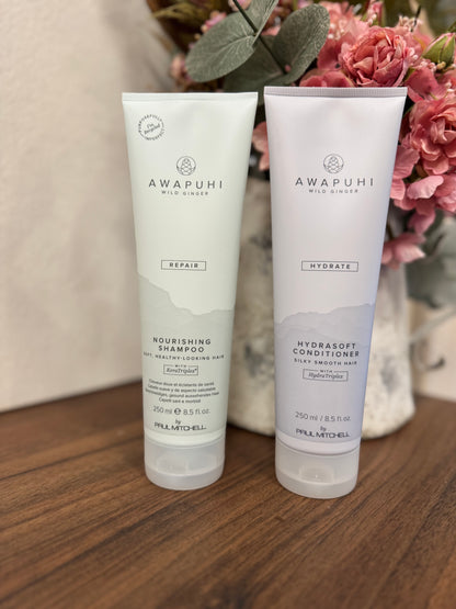 Awapuhi Wild Ginger Shampoo Conditioner Set, zwei Pflegeprodukte auf Holztisch mit Blumen – Paul Mitchell