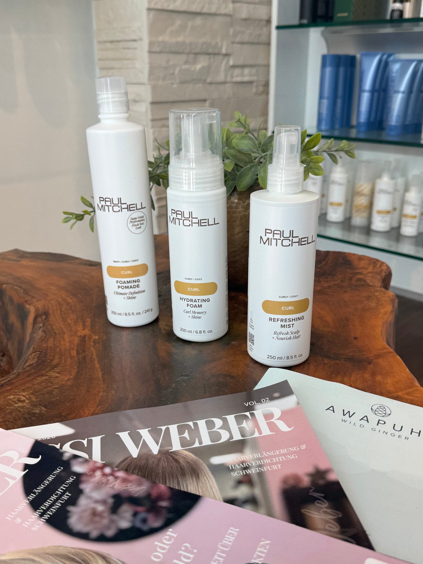     Paul Mitchell Curl Lockenpflege – Foaming Pomade, Hydrating Foam und Refreshing Mist auf Holztisch im Salon – Paul Mitchell