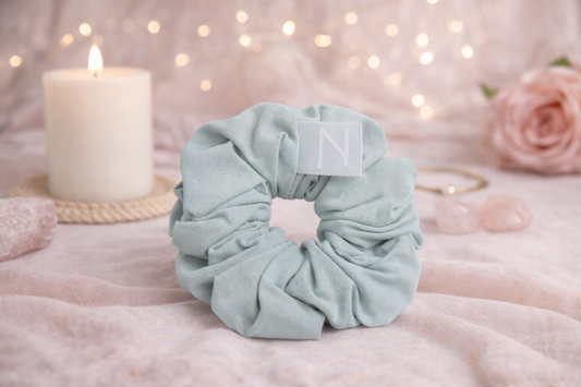 Haarschonender Scrunchie aus Bambusseide dekorativ auf Stoff mit Kerze und sanfter Deko arrangiert