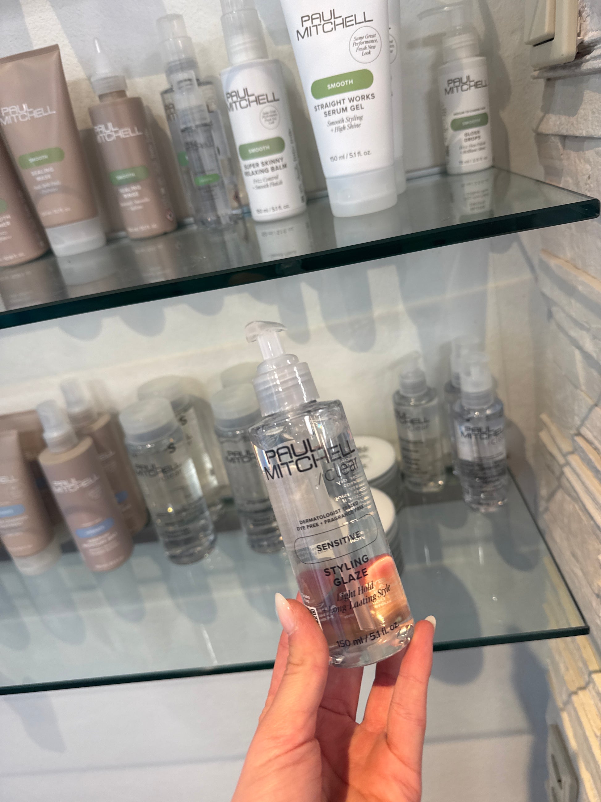 Styling Glaze für empfindliche Kopfhaut mit leichtem Halt in Hand vor Produktregal im Salon – Paul Mitchell