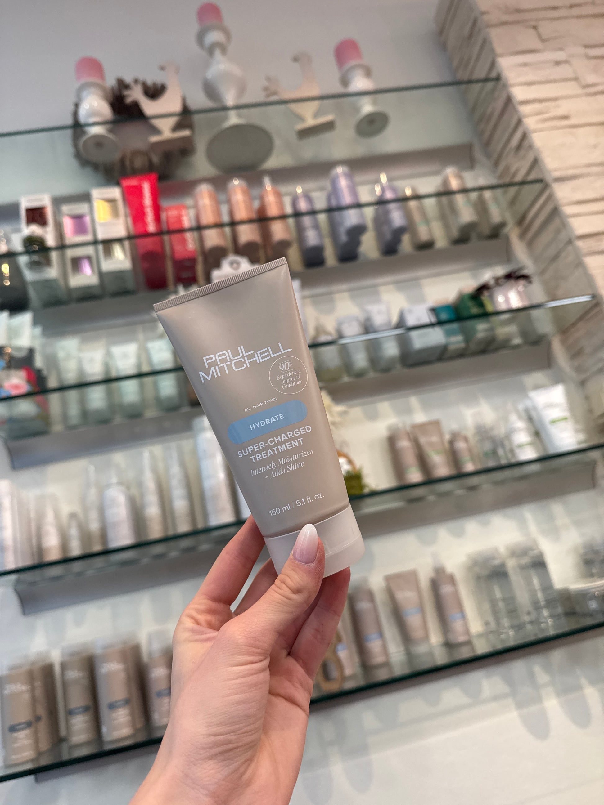 Hydrate Super Charged Treatment Intensivkur für trockenes Haar in Hand vor Produktregal im Salon – Paul Mitchell