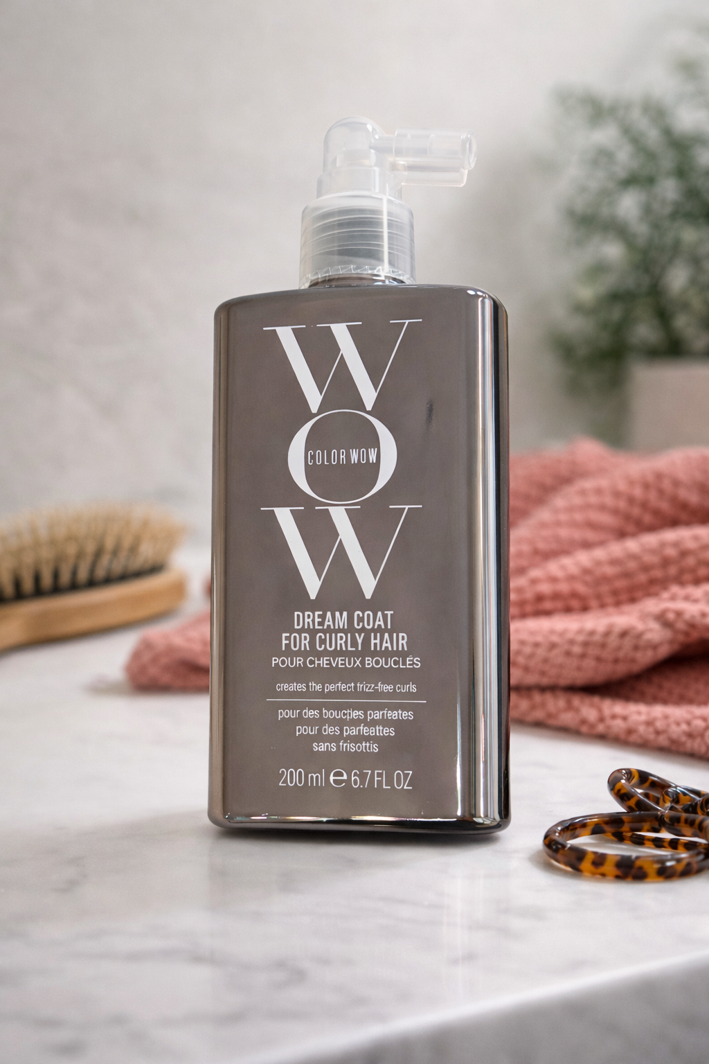 Color Wow Dream Coat for Curly Hair Spray auf heller Oberfläche mit Handtuch und Locken Zubehör – Color Wow