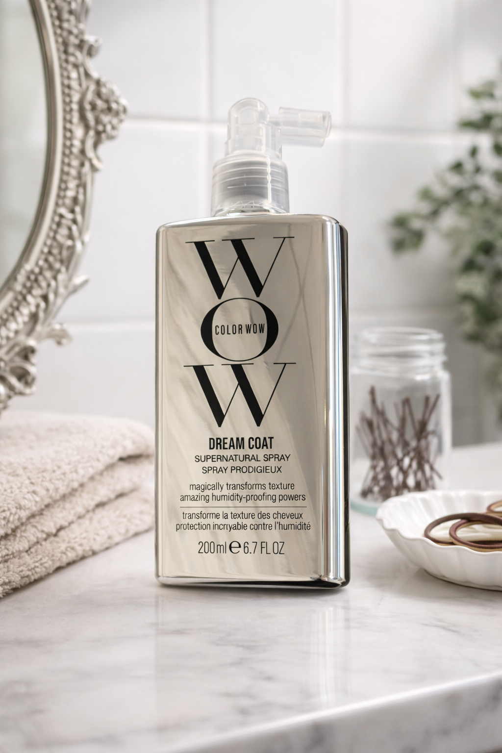 Color Wow Dream Coat Supernatural Spray auf heller Oberfläche mit Handtuch und Haaraccessoires – Color Wow