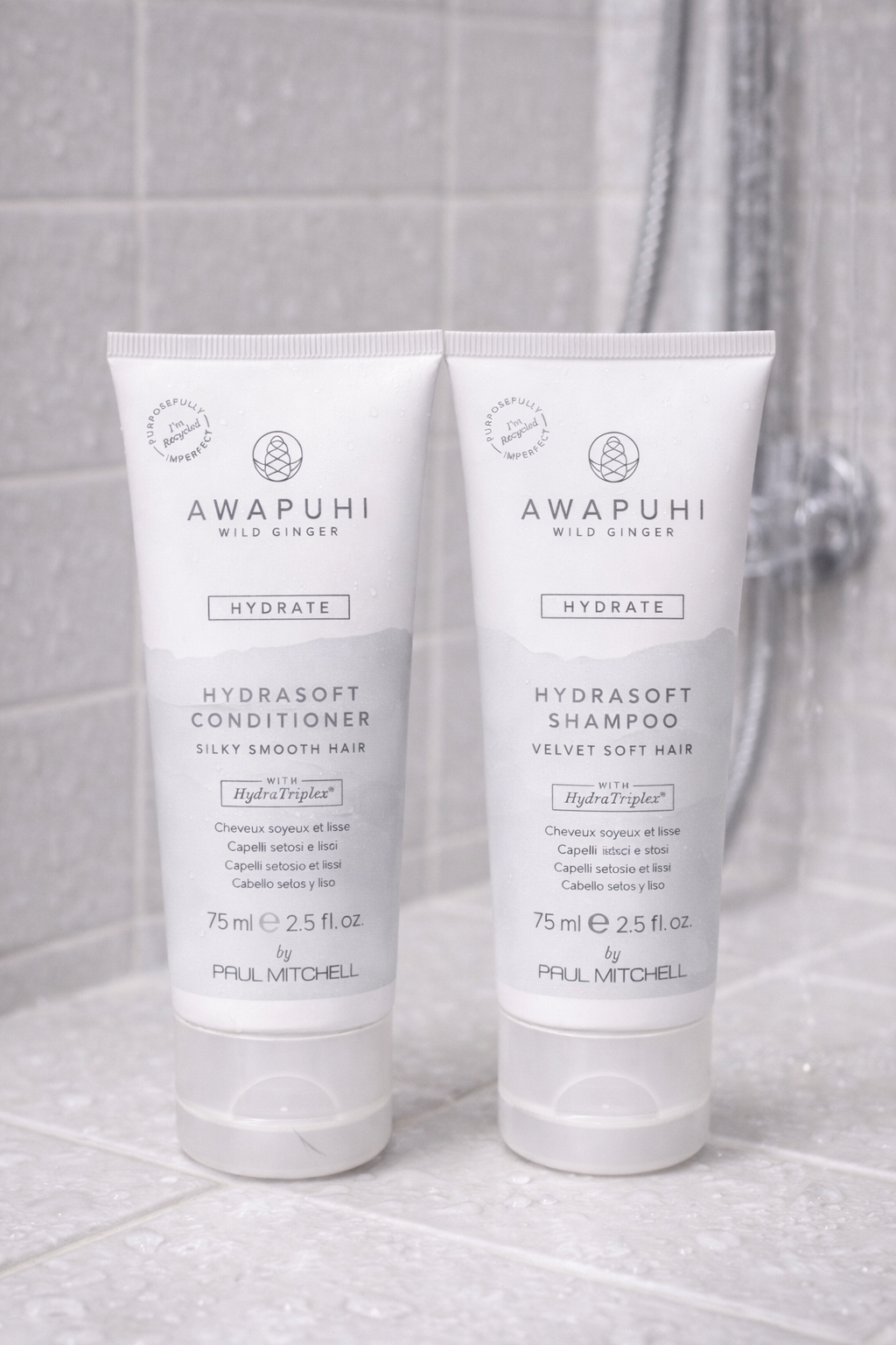 Awapuhi Hydrasoft Shampoo und Conditioner 75 ml, zwei pastellblaue Tuben nebeneinander in Dusche – Paul Mitchell