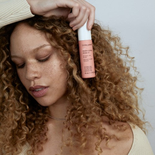Living Proof Curl Moisturizing Shine Oil Model mit lockigem Haar hält Pflegeöl Flasche zur Glanz und Feuchtigkeitsdefinition – Living Proof