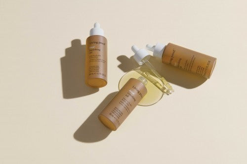 Living Proof Vanishing Oil mehrere Ölflaschen mit Pipette und ausgelaufener Textur auf hellem Untergrund – Living Proof